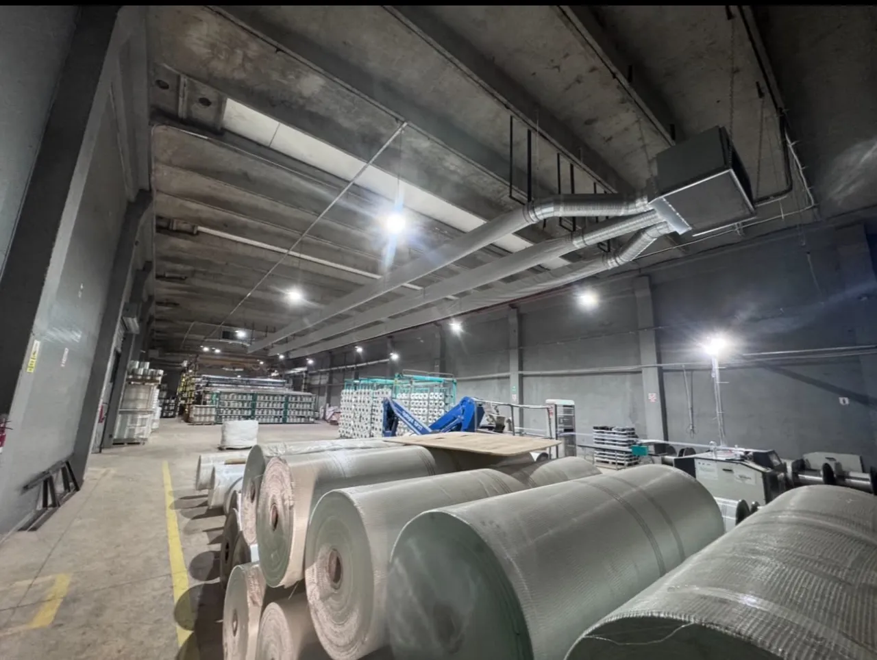 Tubulatură de ventilație la tavanul unei hale înalte, cu role mari așezate pe podea