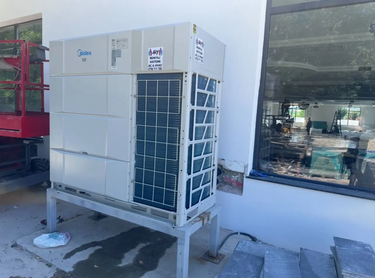 Unitate exterioară Midea VRF pe suport metalic, lângă o fațadă cu geam mare
