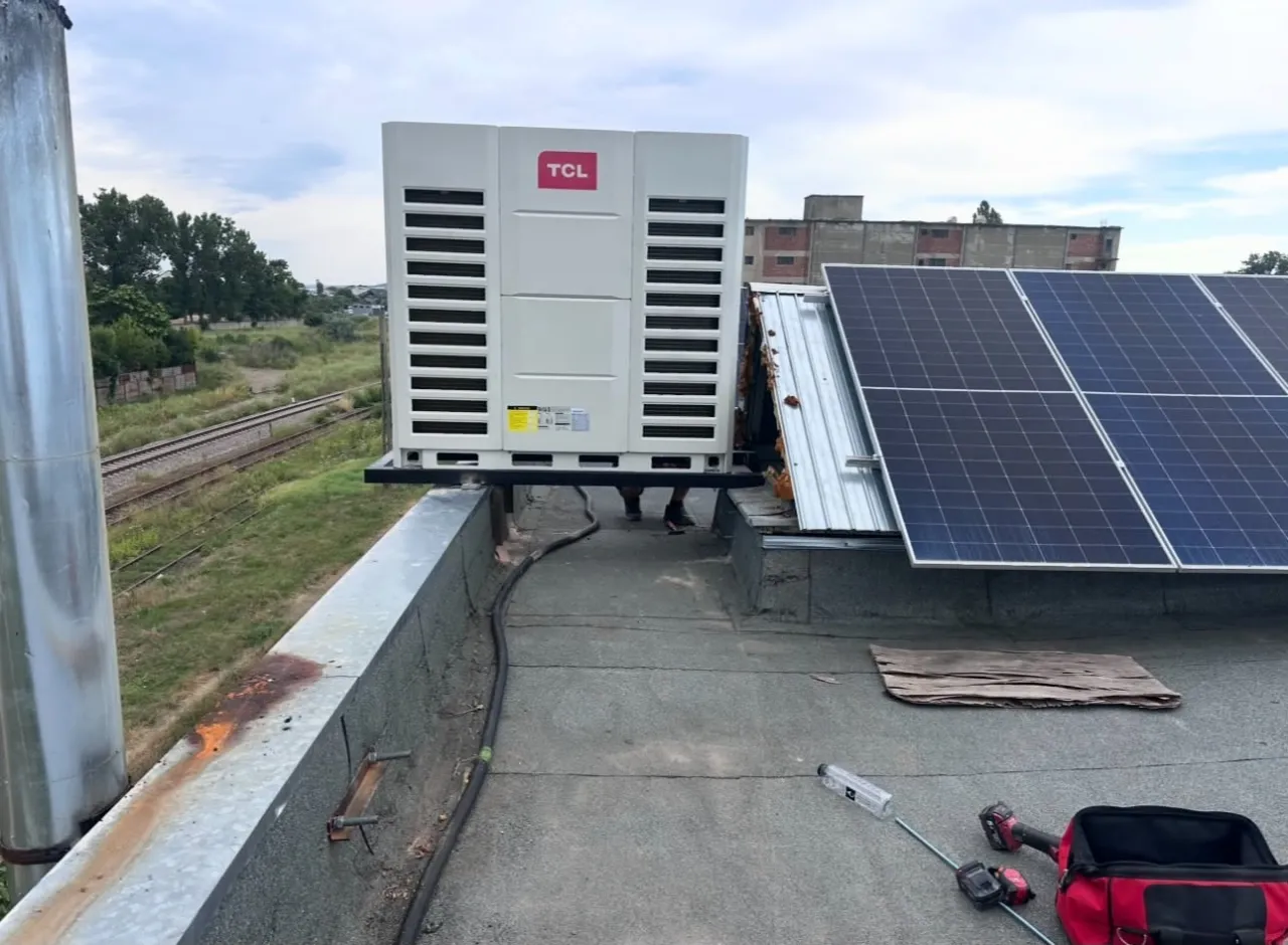 Unitate exterioară TCL pe un acoperiș plat, lângă panouri fotovoltaice, cu o geantă de scule pe jos