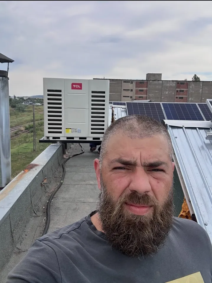 Vlad, în selfie, pe un acoperiș, în fața unei unități exterioare TCL și a panourilor fotovoltaice